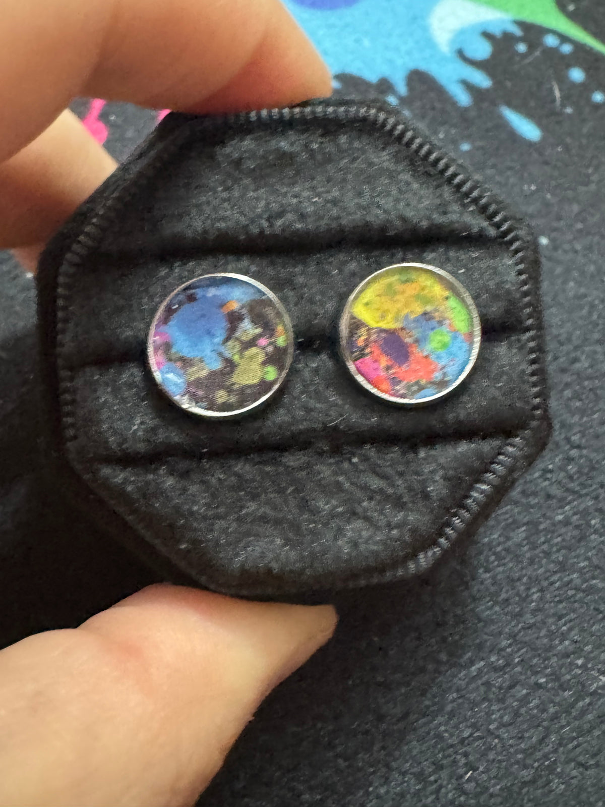 Colorful round earrings in a black hexagonal case held by hands.