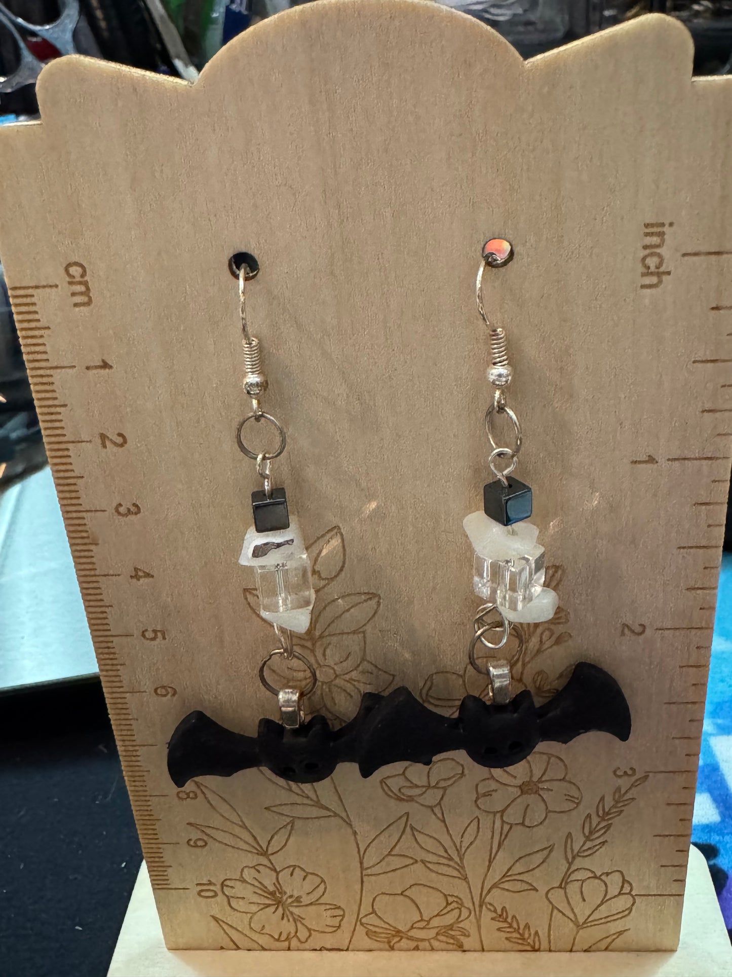 Pair of bat earrings on a wooden display card with measurements.