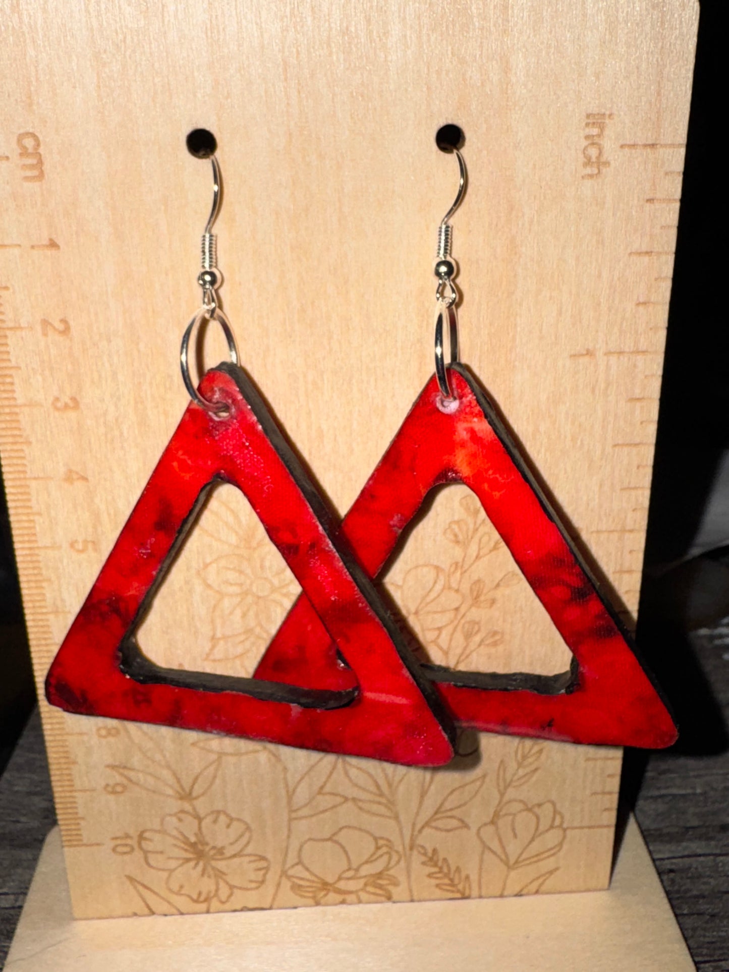 Red triangular earrings on a wooden surface with measurement markings