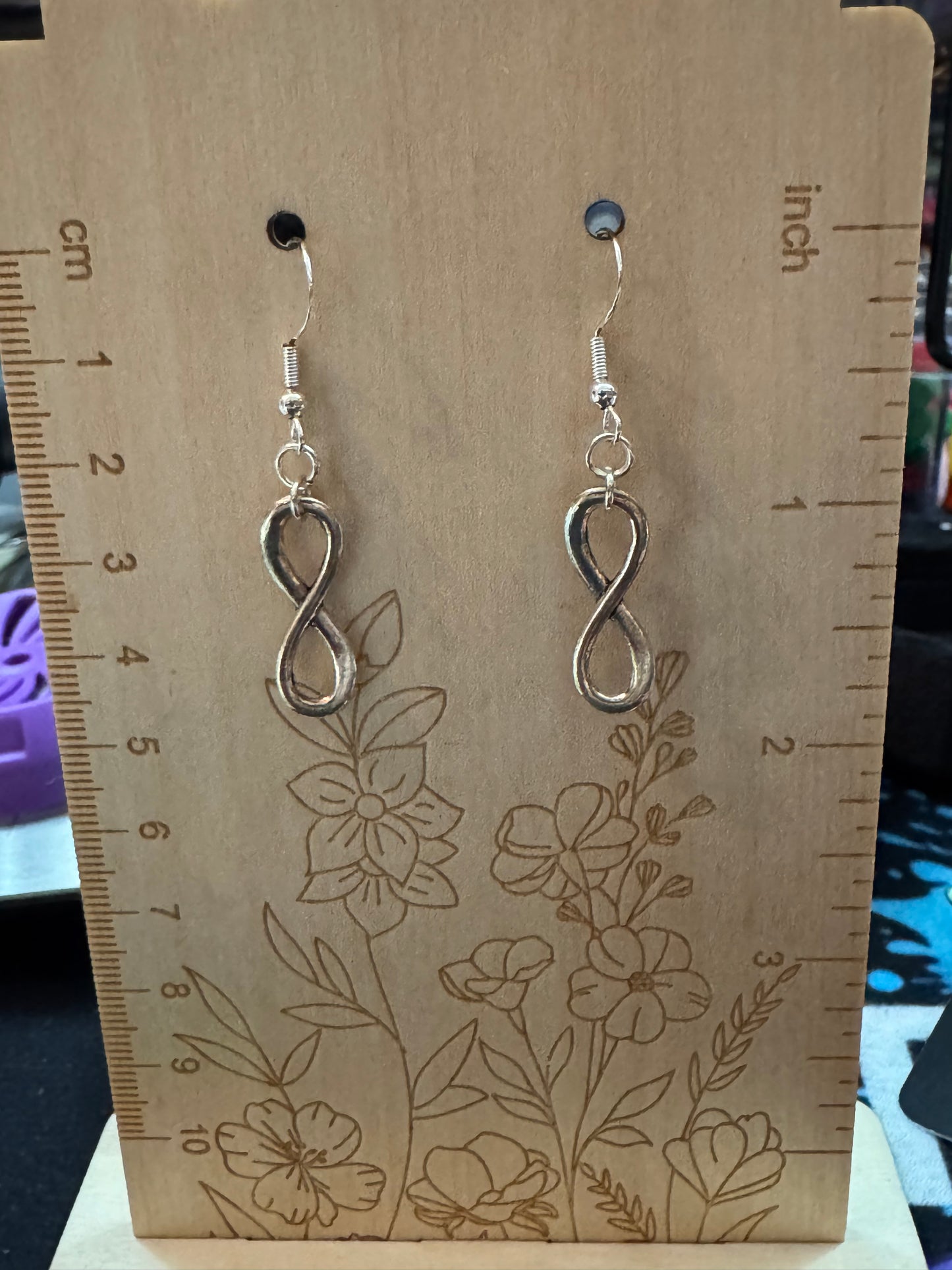 Silver infinity earrings on a floral-patterned card with measurements