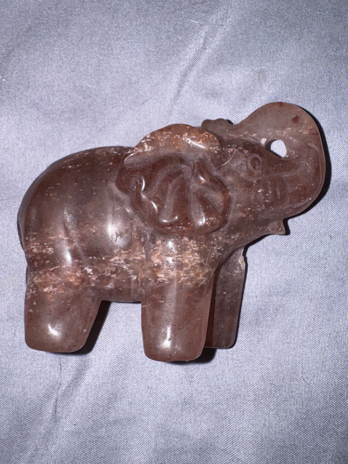 A carved elephant figurine made of polished brown stone, resting on a textured gray fabric background.