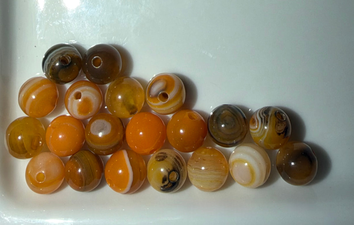 A group of round jasper beads in various natural patterns and colors, including orange, brown, white, and striped designs, arranged on a white surface.