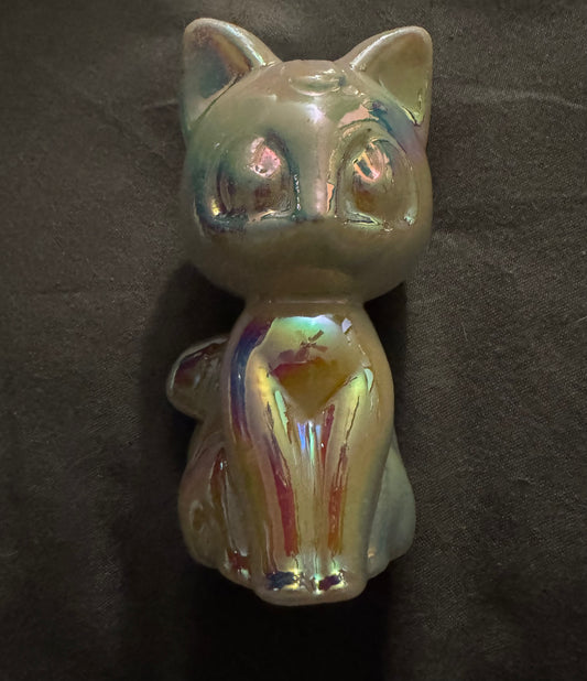 An iridescent cat figurine with a glossy, holographic finish, sitting on a dark textured background.