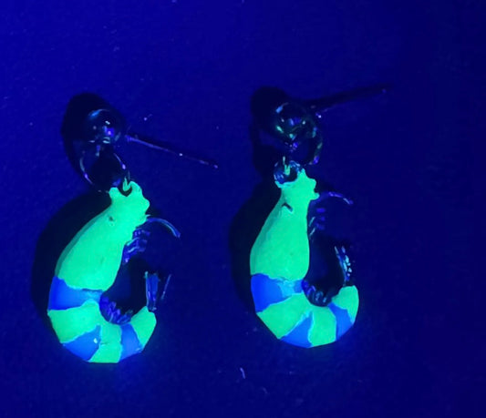 Glowing green and blue earrings under a black light on a dark background
