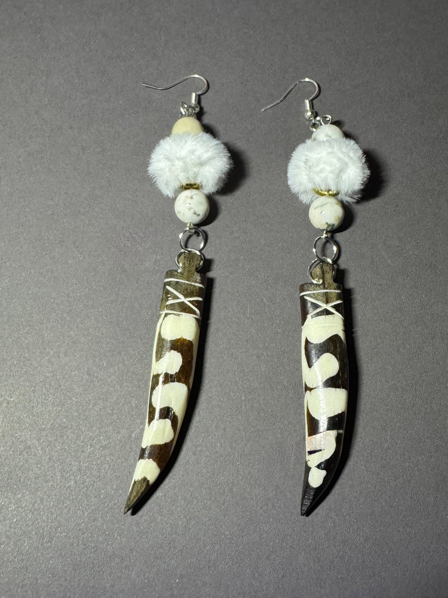 A pair of handmade dangle earrings featuring brown and white cowhide horn blades with white bead details and fluffy white faux fur, displayed on a neutral gray background.