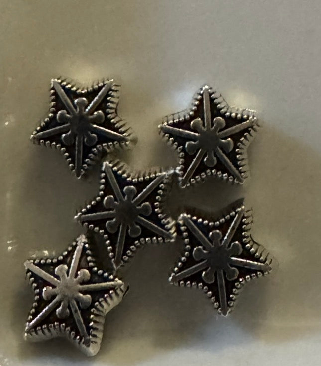 Five silver-toned star-shaped stud earrings with textured beaded edges, arranged on a light beige surface.