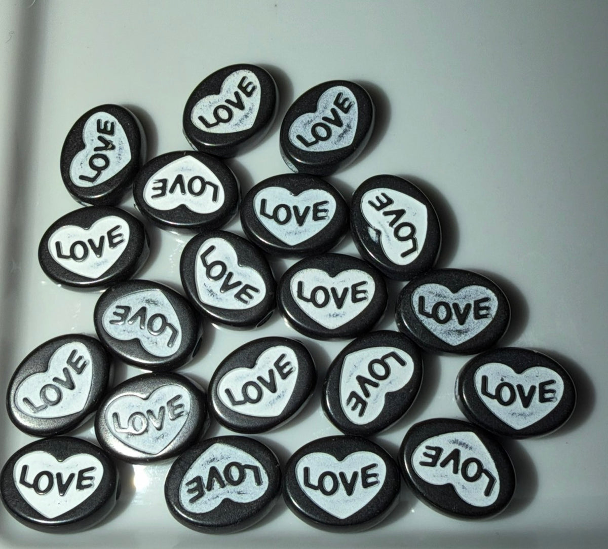 A pile of small black heart beads, each featuring a white heart in the center with the word 'LOVE' printed inside.