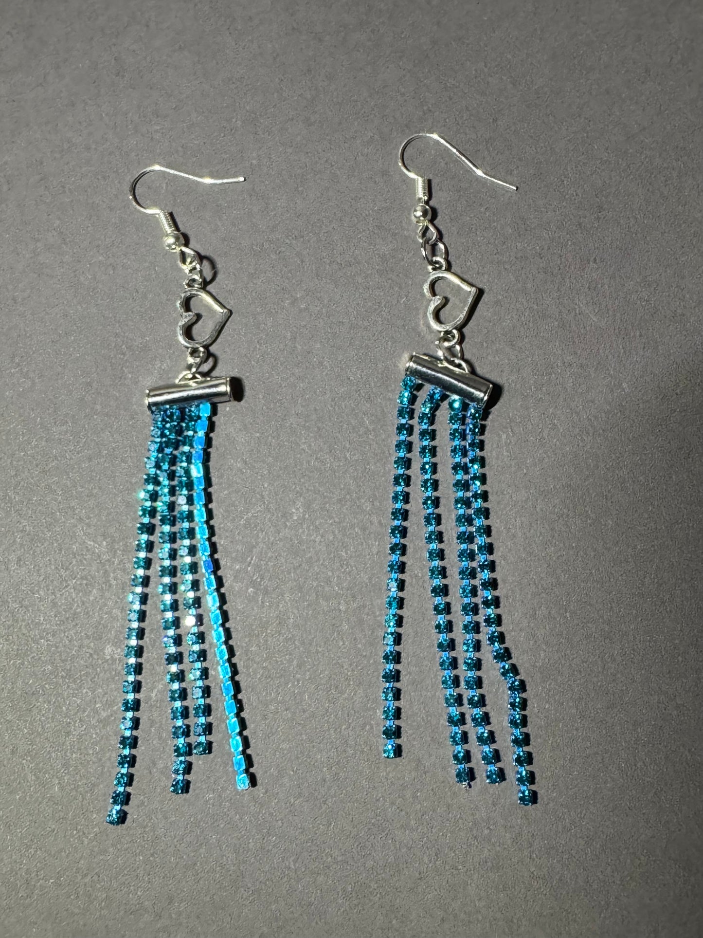 A pair of dangling earrings with silver fishhook wires and multiple strands of small blue beads, photographed on a plain gray background.