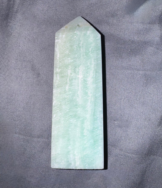 A natural light green amazonite crystal point stake with a smooth, polished surface, standing upright on a textured gray fabric background.