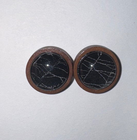 A pair of round wooden button covers with a black stone inlay featuring white veining, set against a plain off-white background.