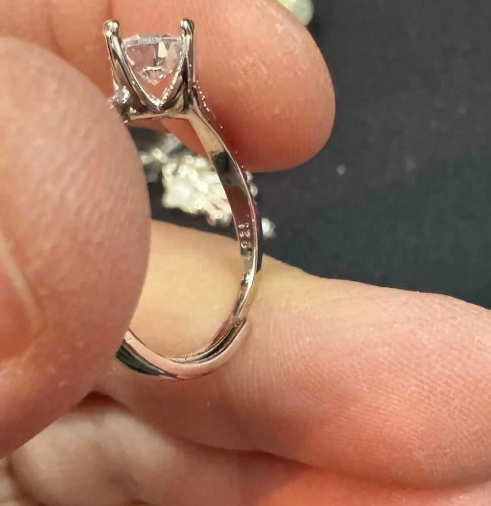 Silver ring with a diamond on a finger against a dark background