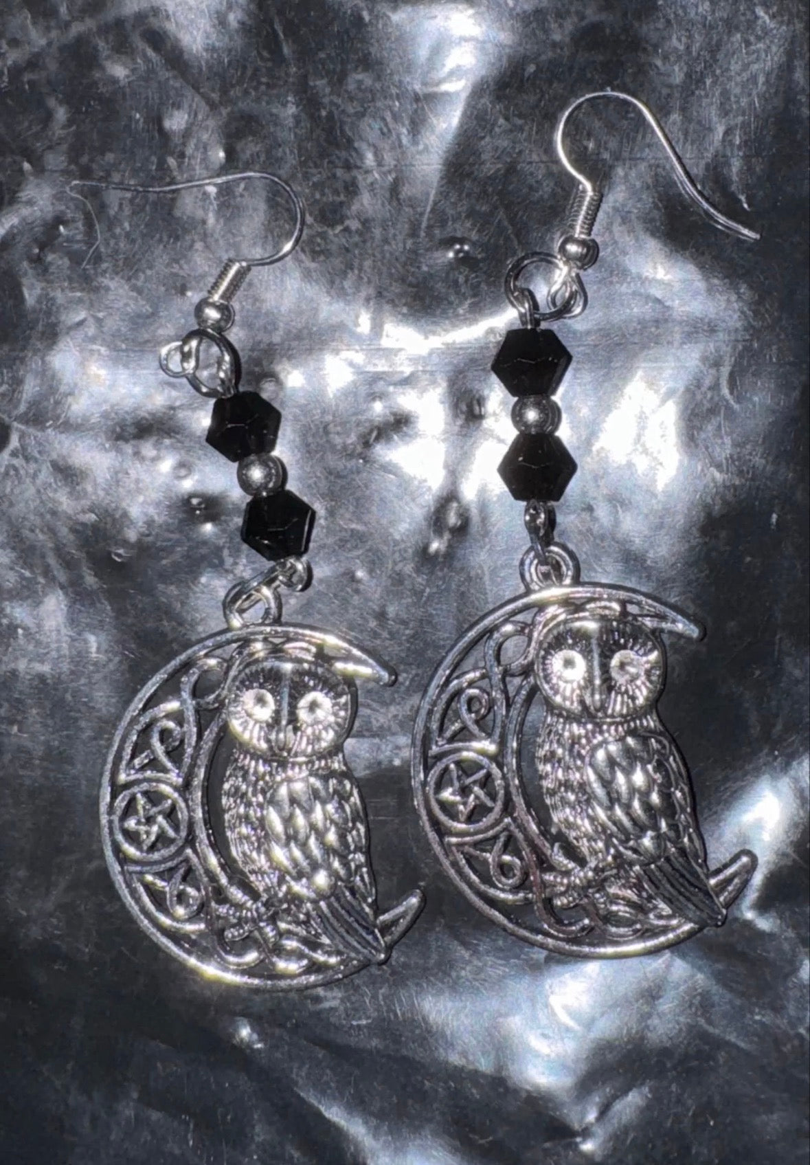 Silver owl earrings with black beads on a metallic surface