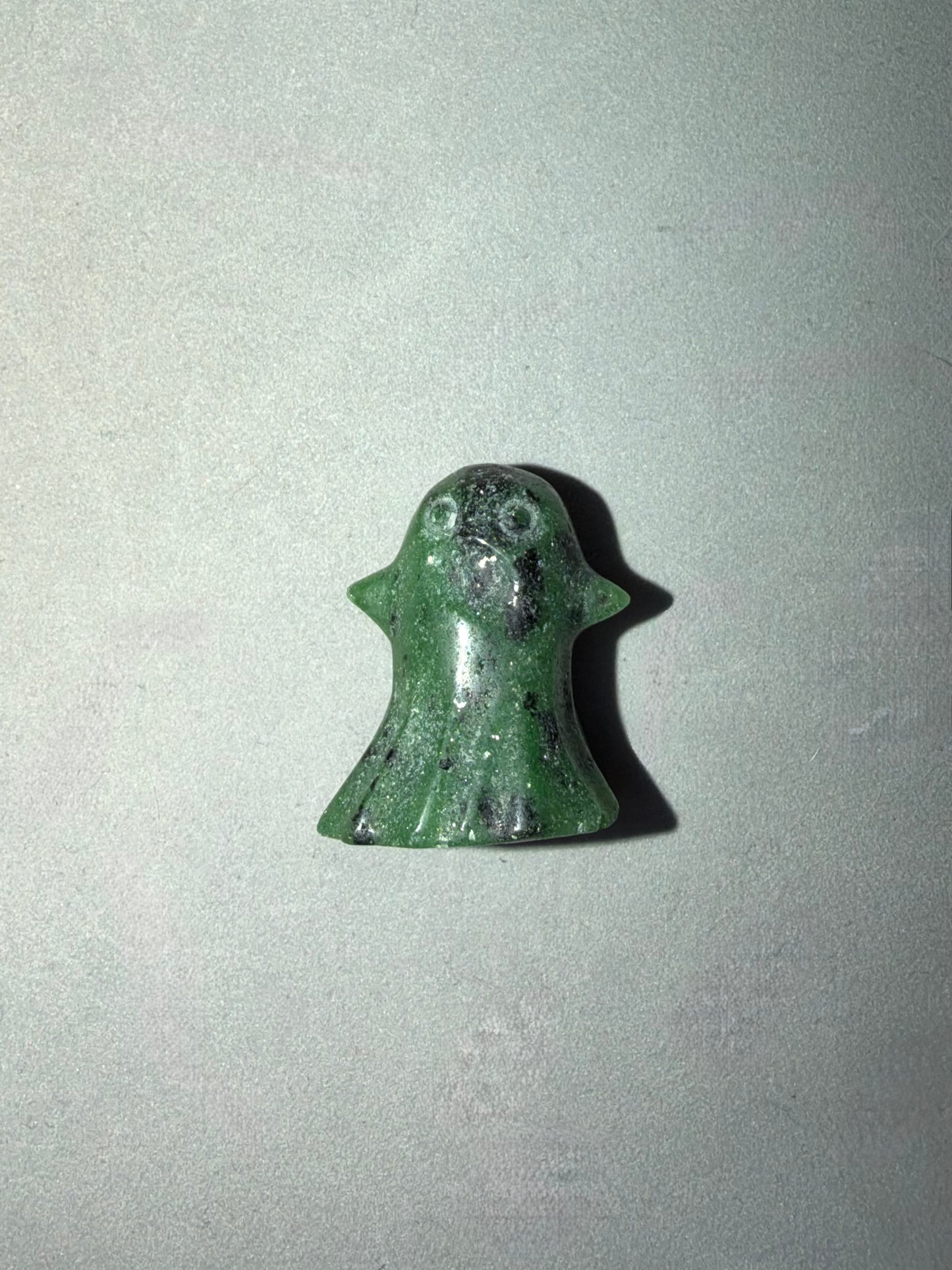 A small green ghost-shaped carved stone or resin charm with a glossy finish, shown on a plain light gray background.