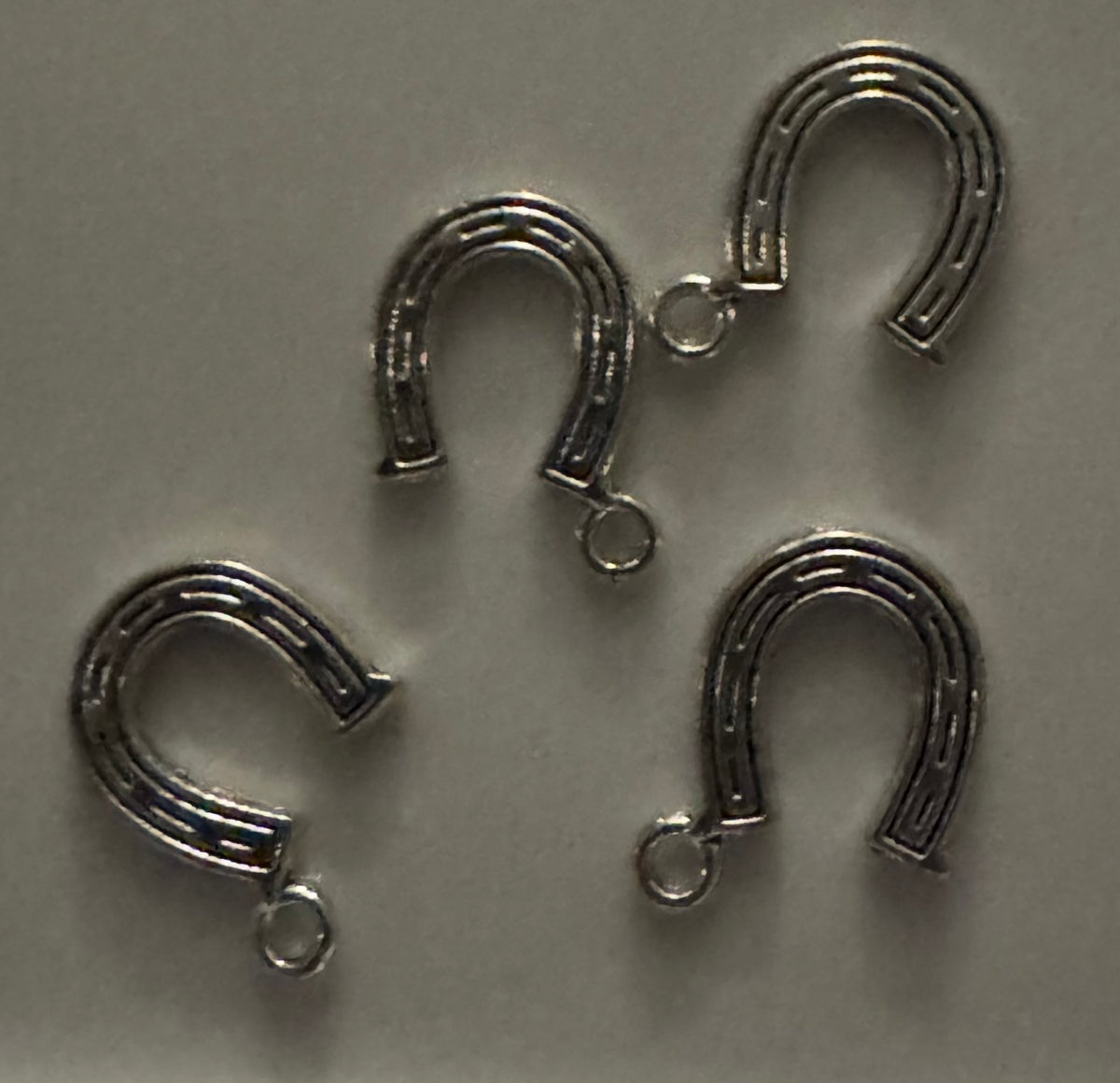 Five silver horseshoe-shaped jewelry charms with attached jump rings, arranged on a plain light gray background.