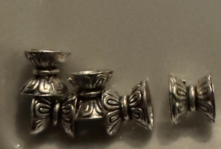 Five silver-toned metal spacer beads with ornate floral engravings, displayed on a neutral gray background.