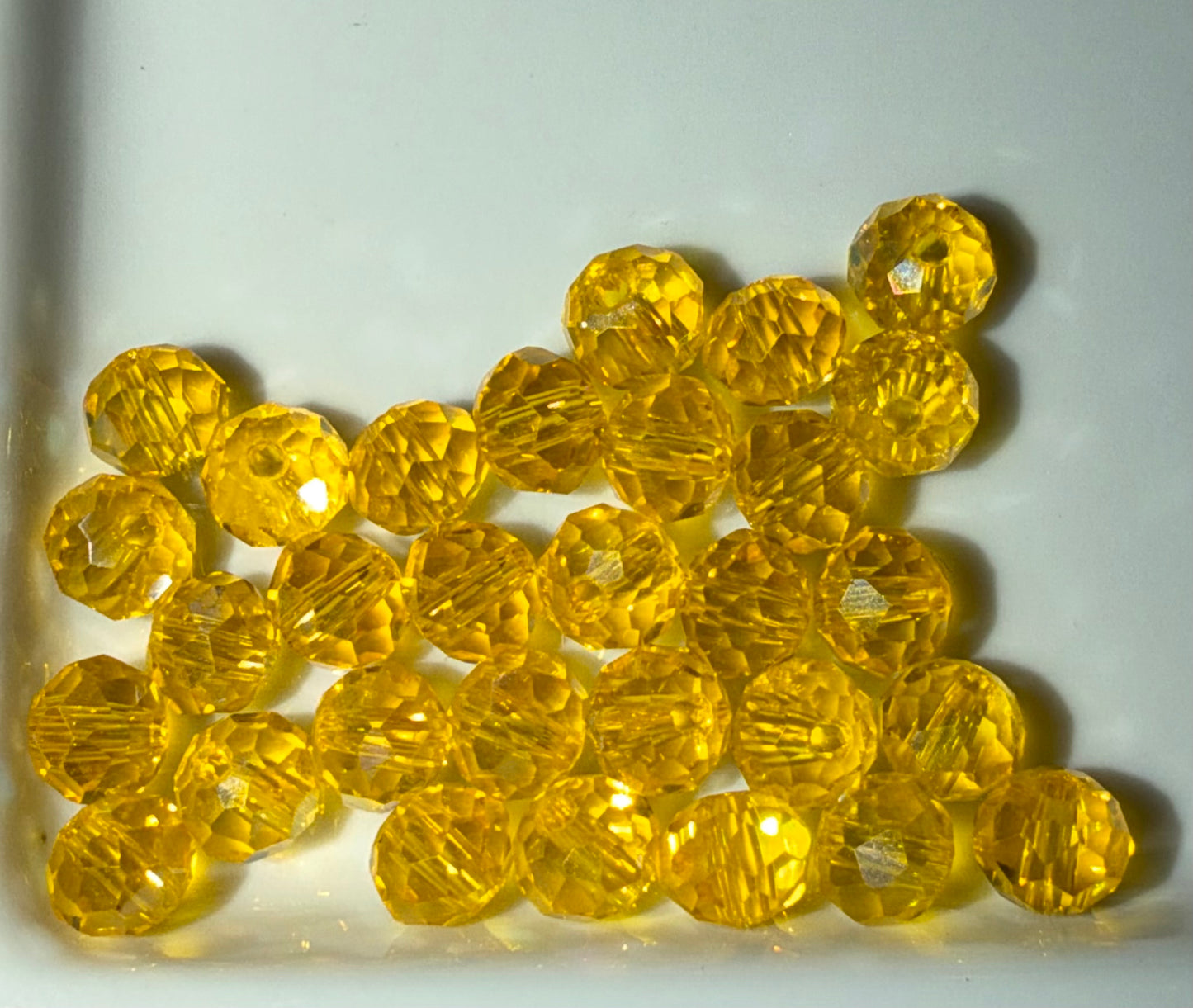 A pile of faceted yellow glass beads with a clear, transparent appearance, resting on a plain white surface.