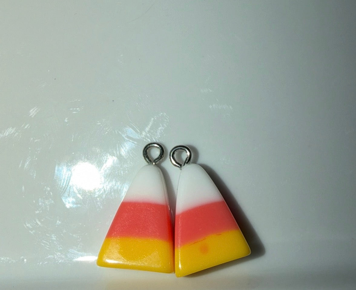 Two triangular candy corn charms with silver jump rings, featuring white, orange, and yellow horizontal stripes, on a light gray background.
