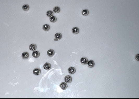 Several small metallic silver dome beads scattered on a plain white surface.