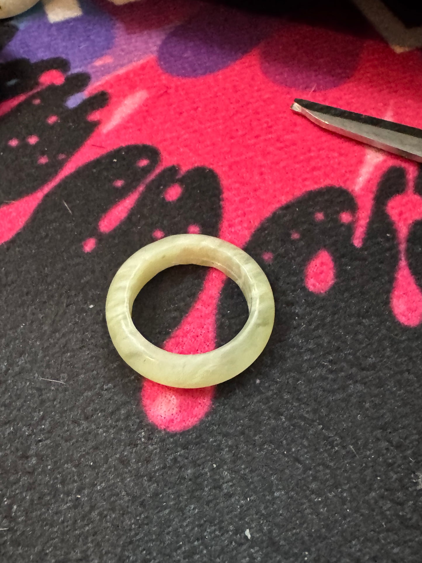 Jade ring on a black and pink textured surface with tweezers