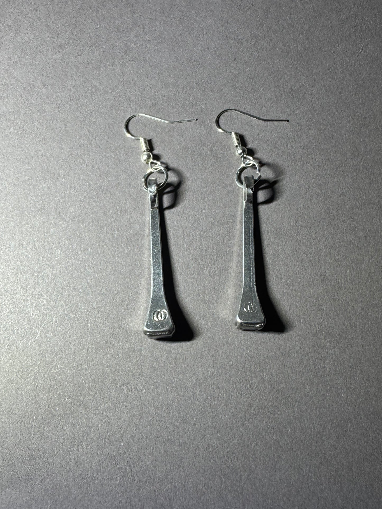 A pair of silver-toned drop earrings with elongated rectangular pendants and fishhook ear wires, photographed on a plain gray surface.