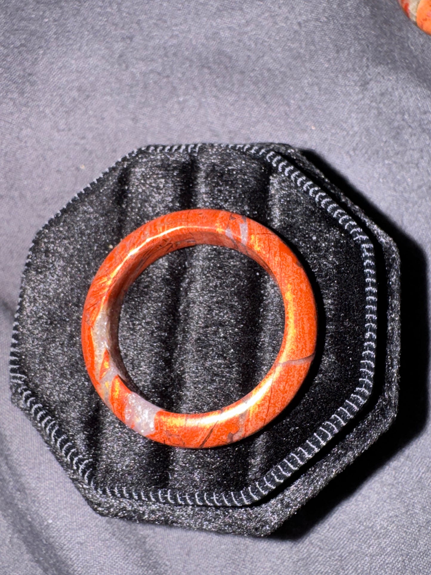 Red stone ring on a black hexagonal stone with a gray fabric background