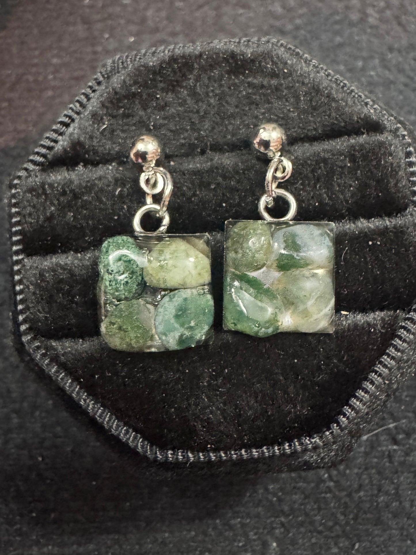 Pair of moss agate stone earrings on a black velvet stand.