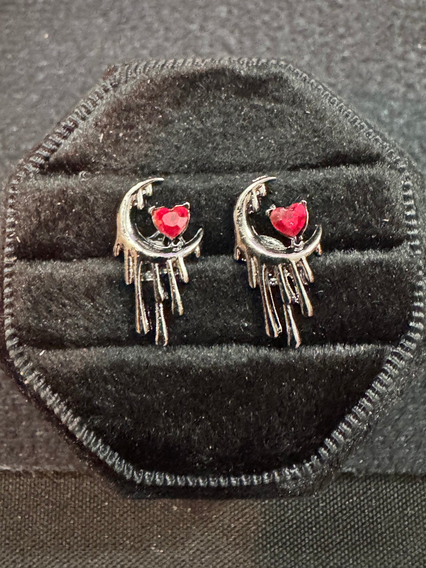 Pair of earrings with crescent moon and heart design on a black velvet cushion