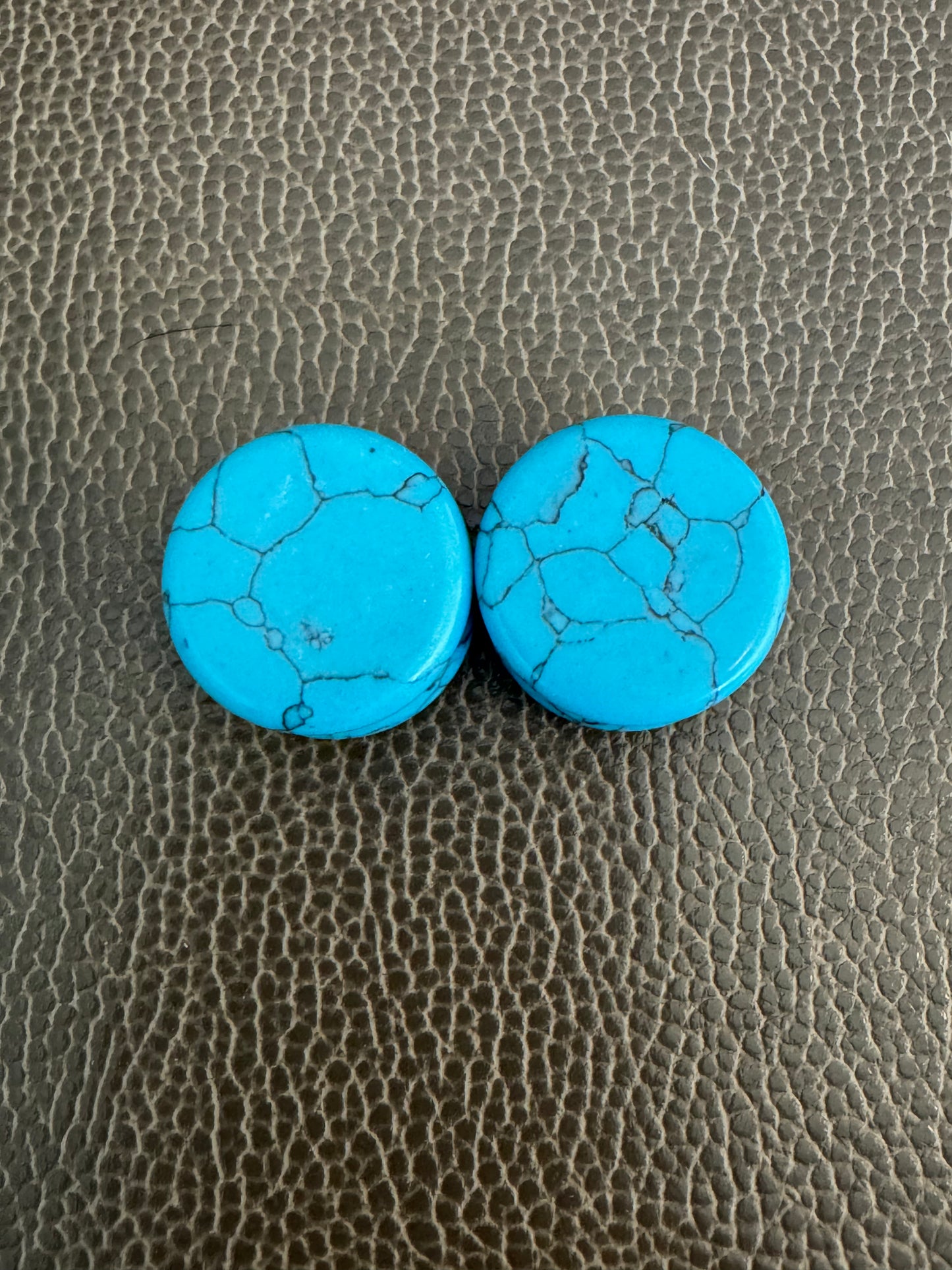 Two turquoise stone earrings on a textured brown surface