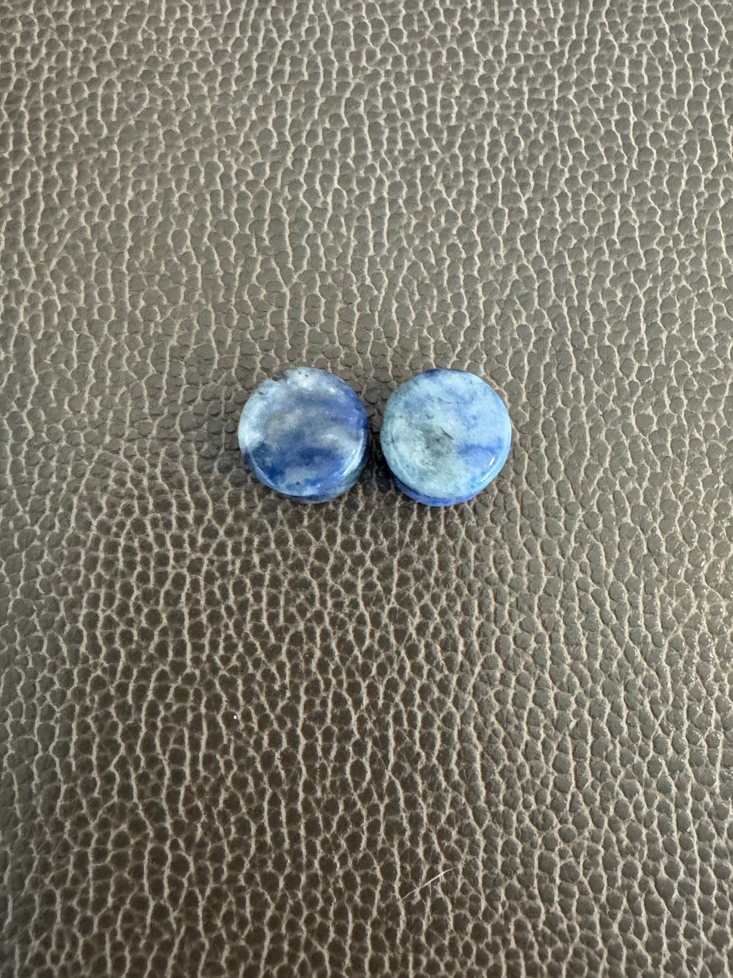 Two blue spot Jasper ear gauges on a textured brown surface