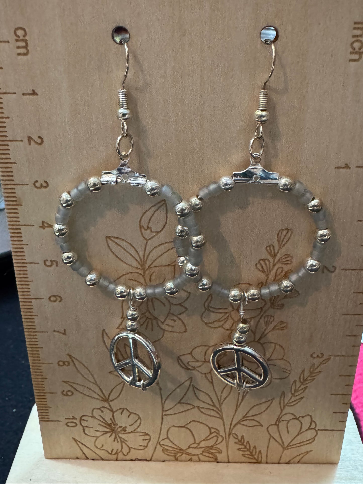 Silver earrings with peace sign charms on a floral-patterned card with a ruler for scale.