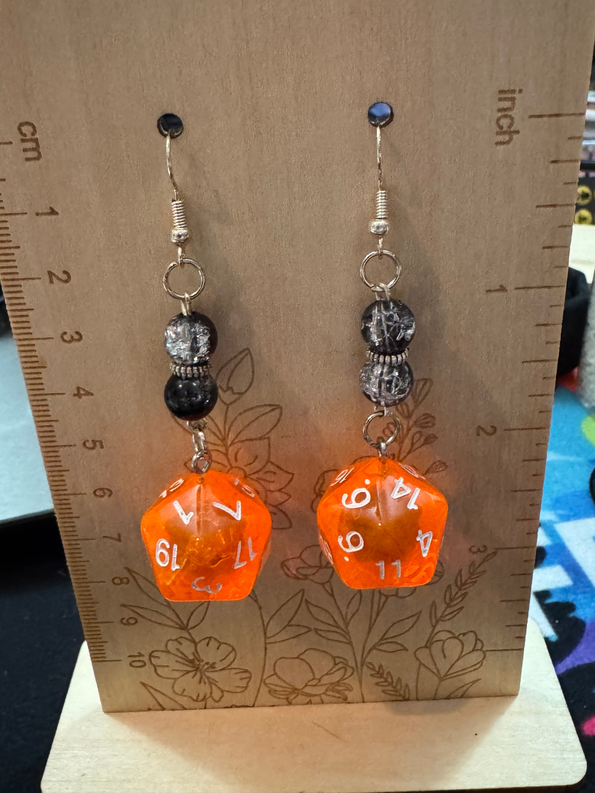 Orange dice-shaped earrings on a wooden surface with a ruler for scale.