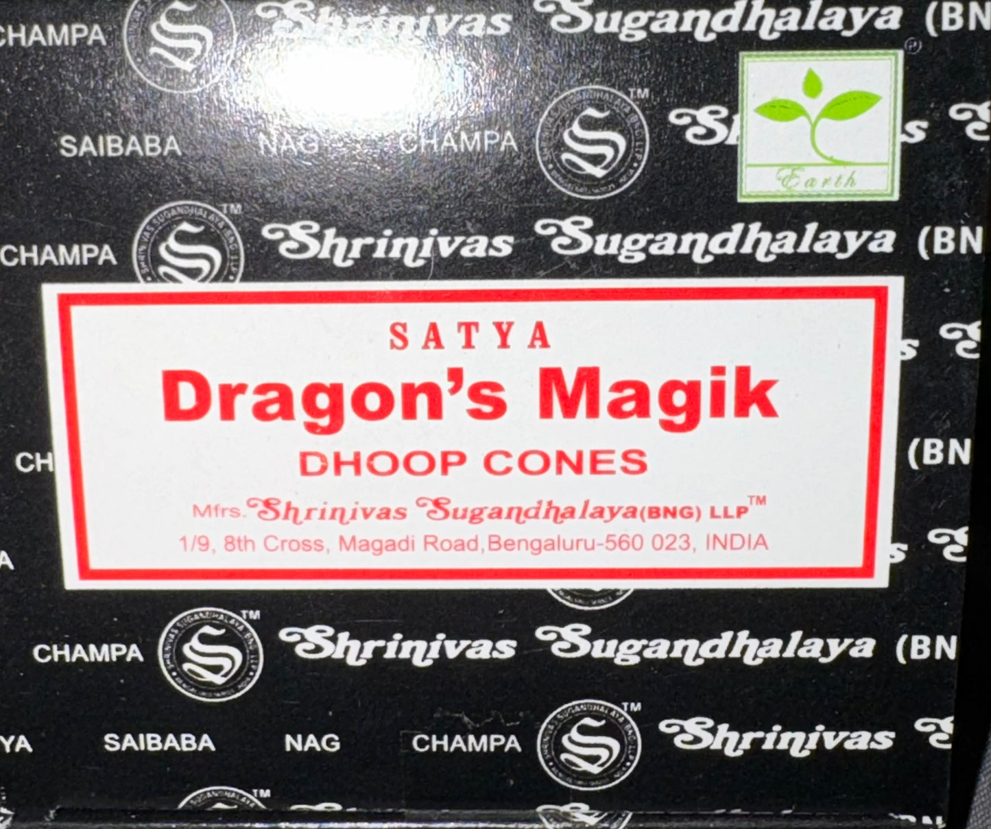 A close-up of a black box of Satya Dragon's Magik Dhoop Cones by Shrinivas Sugandhalaya, featuring a white label with red text and a black background with repeating white brand logos.