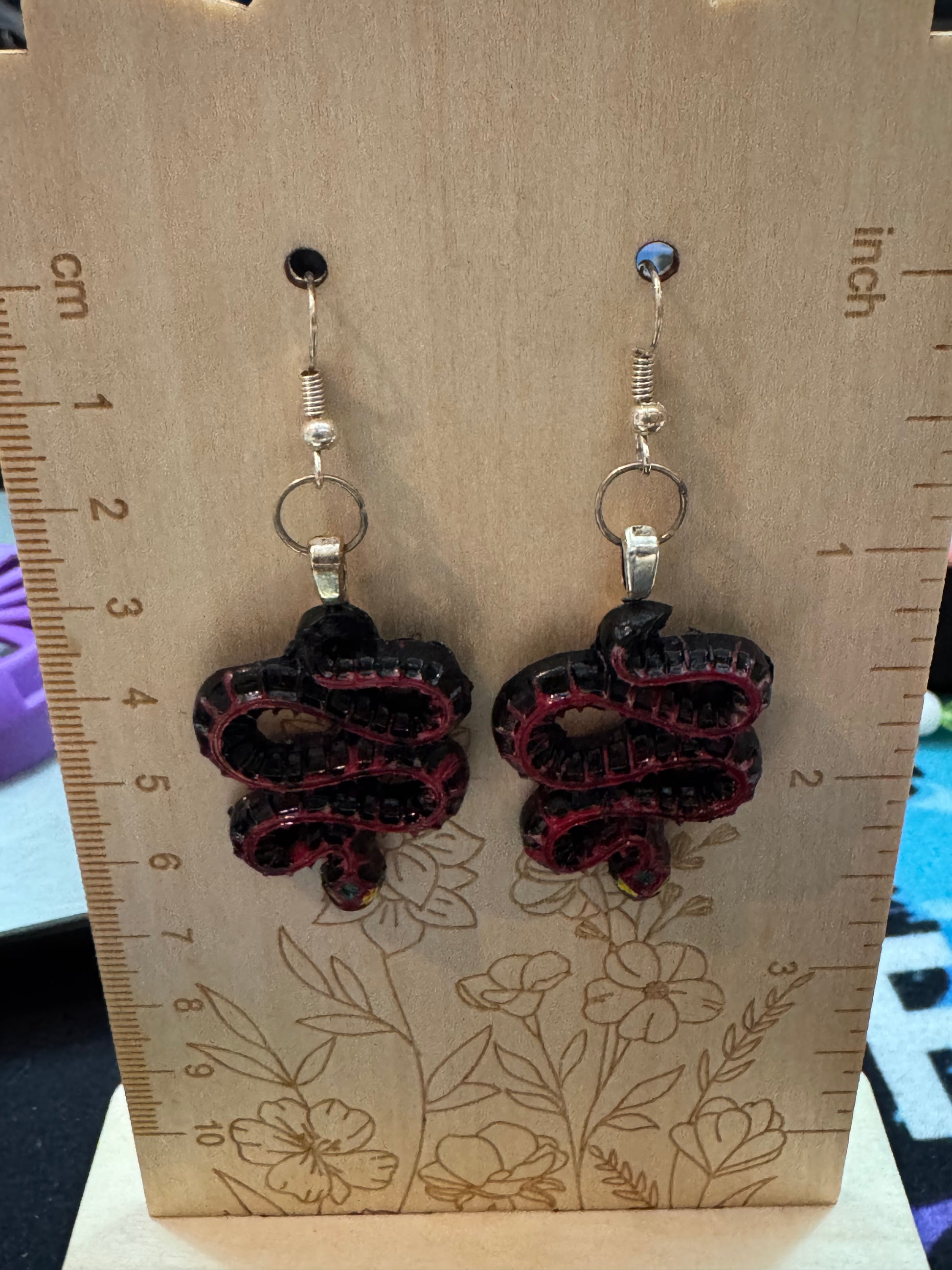 Pair of snake earrings on a wooden card with measurements.