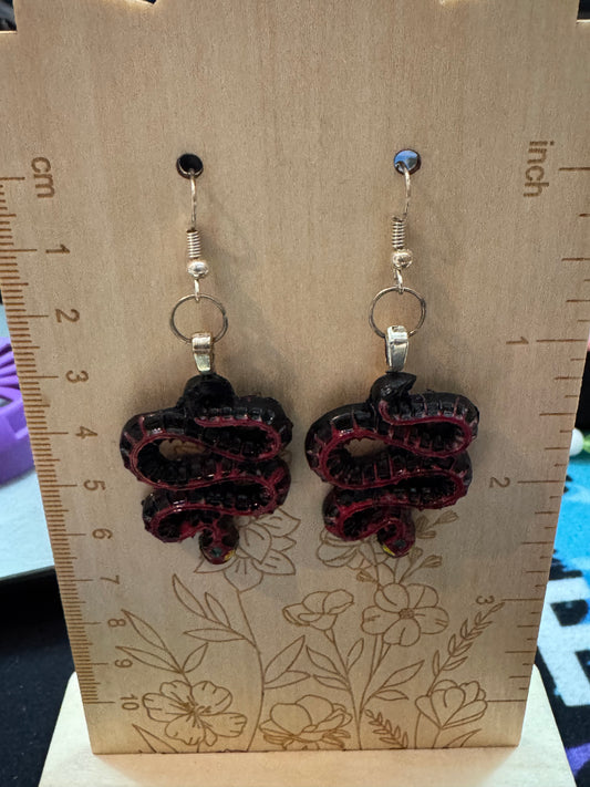 Pair of snake earrings on a wooden card with measurements.