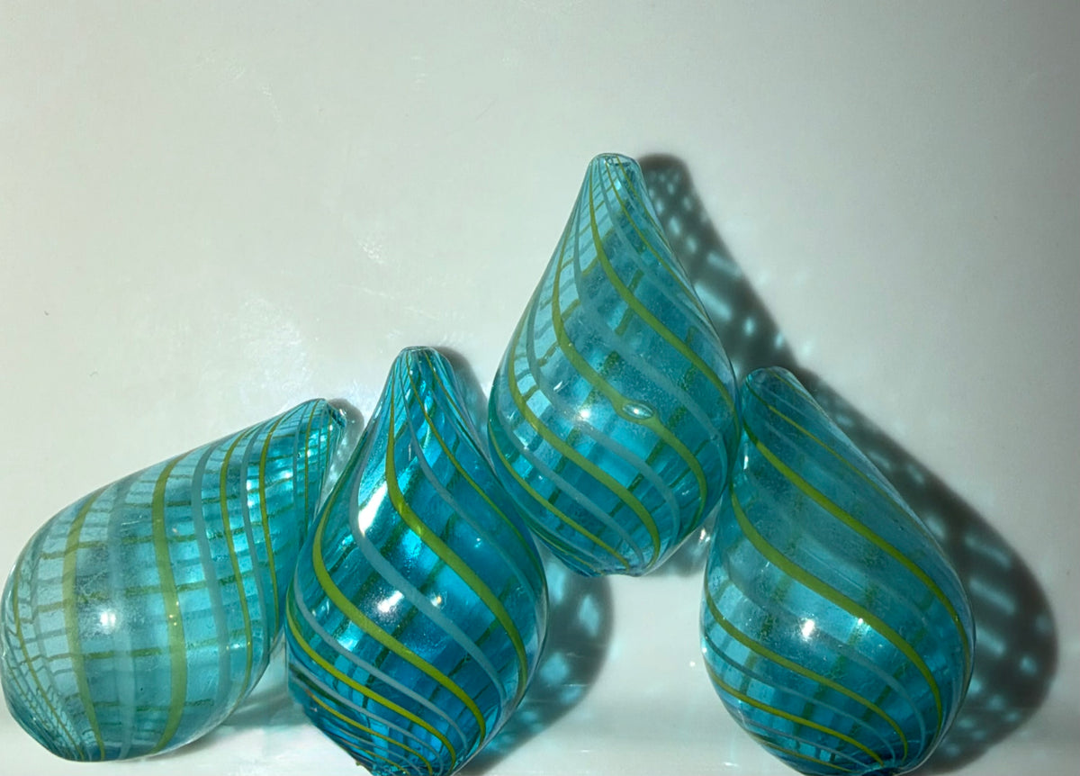 Four teardrop-shaped glass beads in shimmering turquoise blue with yellow-green swirls, displayed on a light off-white background.