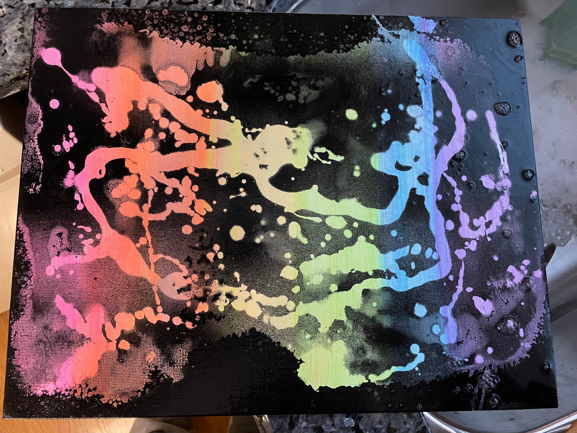 Abstract black spray-paint splattered canvas with vibrant neon streaks of pink, orange, yellow, green, blue, and purple.