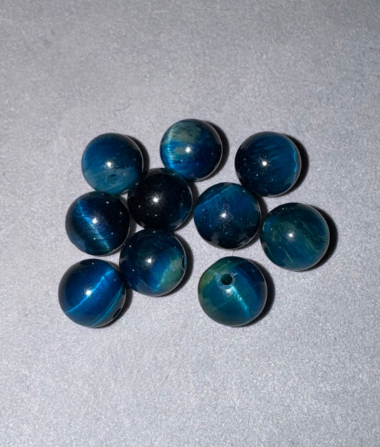 Nine round blue tigers eye beads with a central hole, arranged on a light gray textured background.