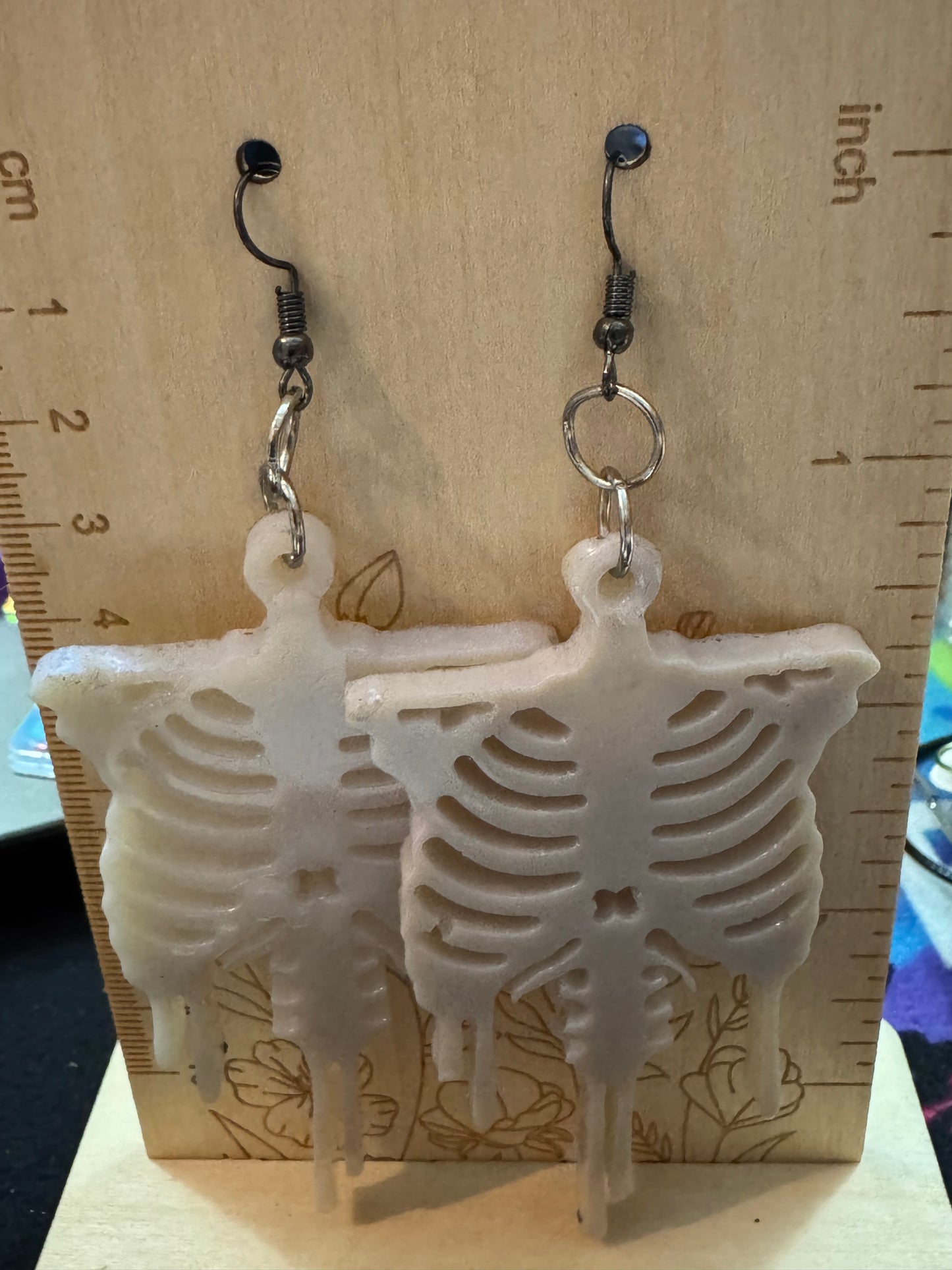 Skeletal design earrings on a wooden surface with a ruler for scale.
