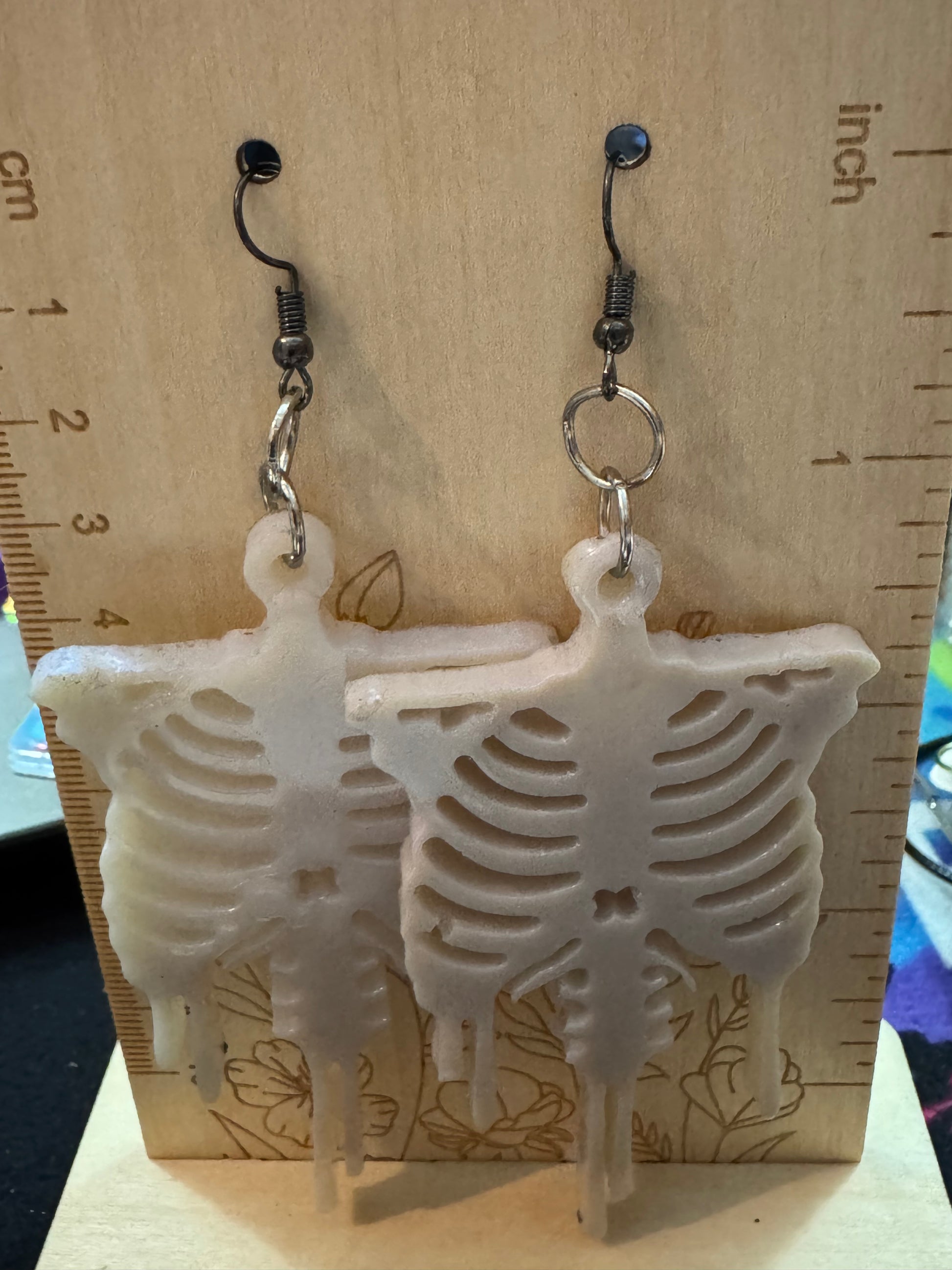 Skeletal design earrings on a wooden surface with a ruler for scale.