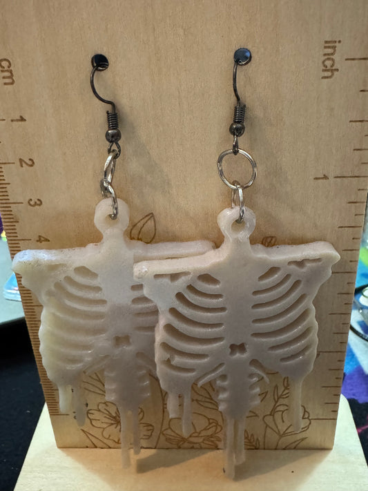Skeletal design earrings on a wooden surface with a ruler for scale.