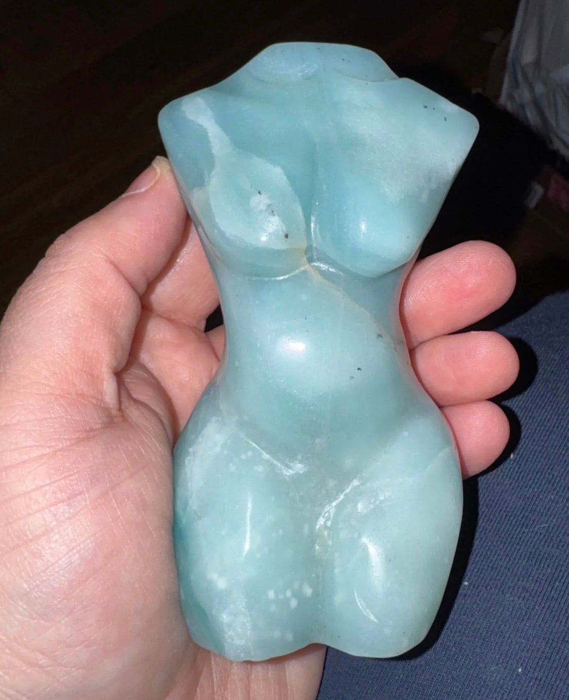 Hand holding a light blue stone sculpture of a torso.