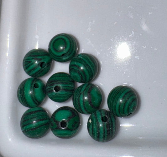 Nine green malachite beads with natural banded patterns and central holes, arranged on a white ceramic dish.