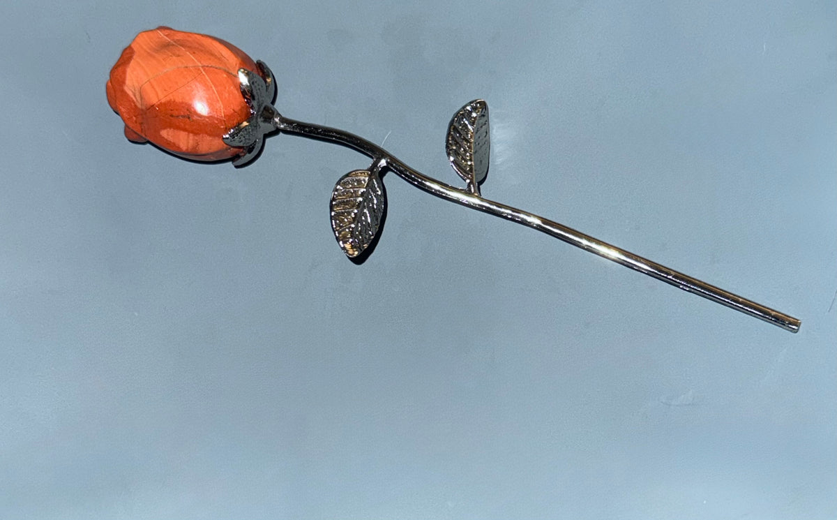 A silver-toned rose with a polished orange stone flower head, set against a plain light blue background.