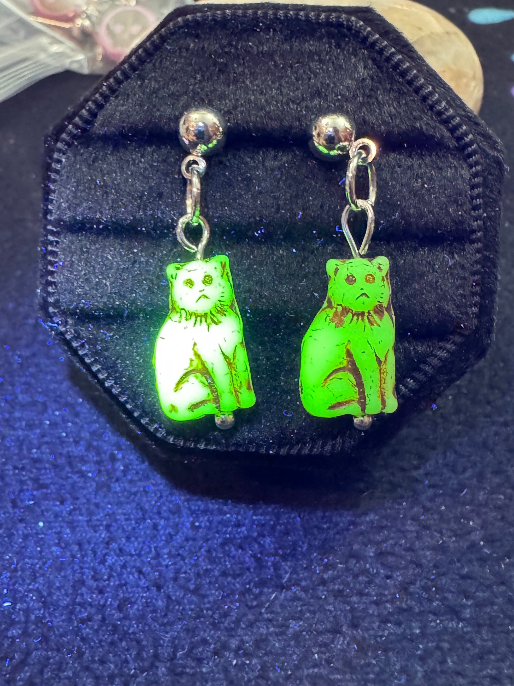 Green ghost-shaped earrings in a black jewelry case on a dark blue background