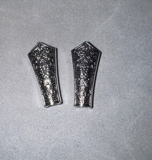 Two silver-toned metal decorative pieces with intricate floral engravings, displayed side-by-side on a textured gray background.