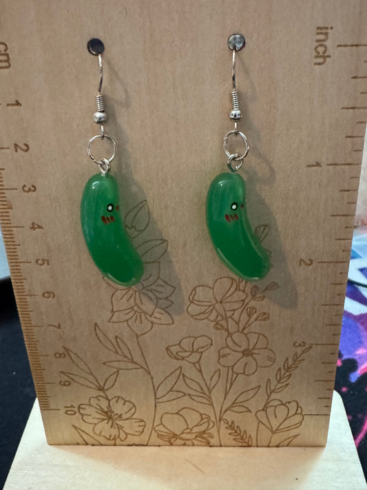 Two pickle earrings on a wooden board with floral patterns and a ruler for scale.