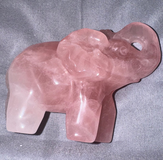 A carved pink rose quartz elephant figurine resting on a textured gray fabric background.
