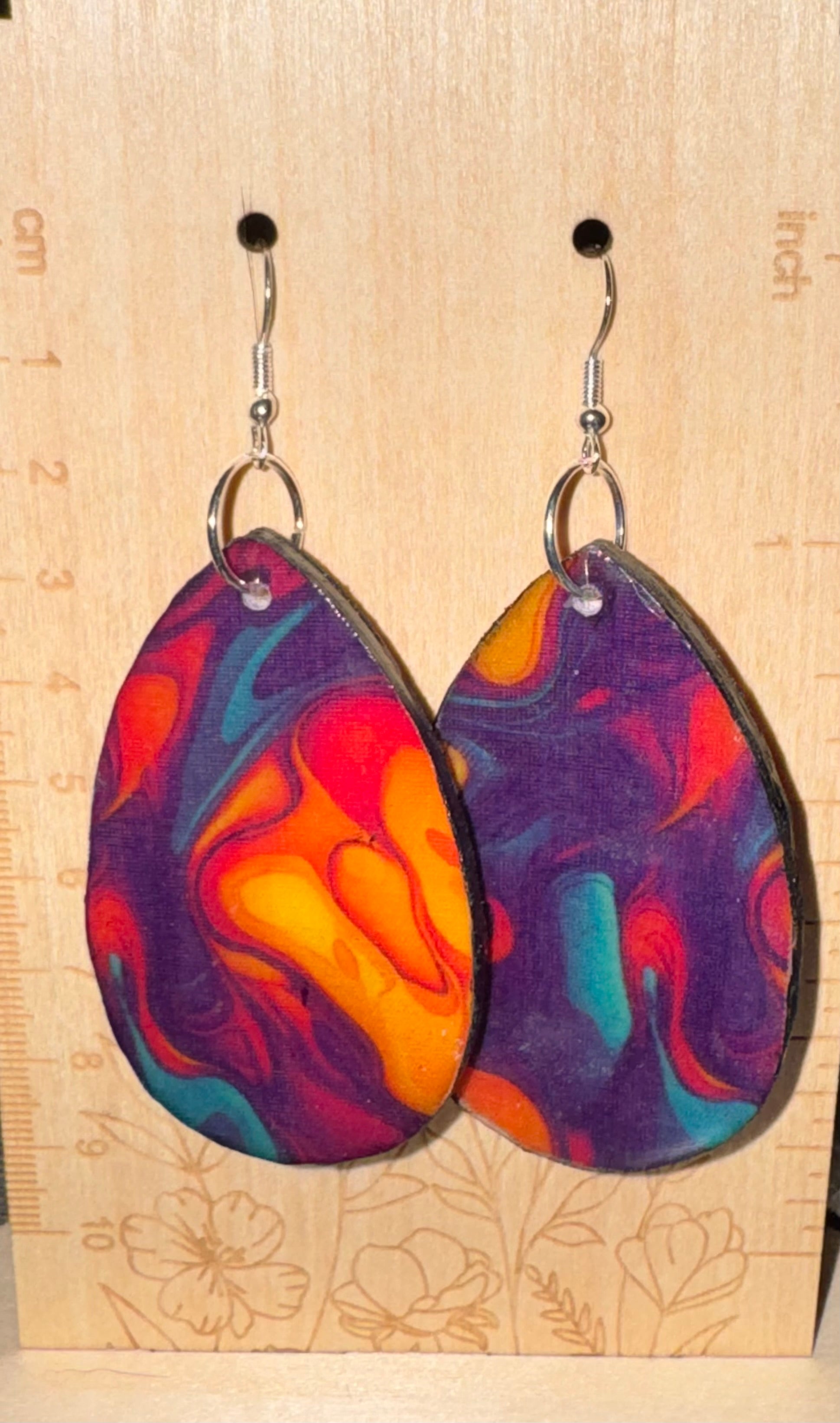 Colorful teardrop earrings on a wooden surface with measurement markings.