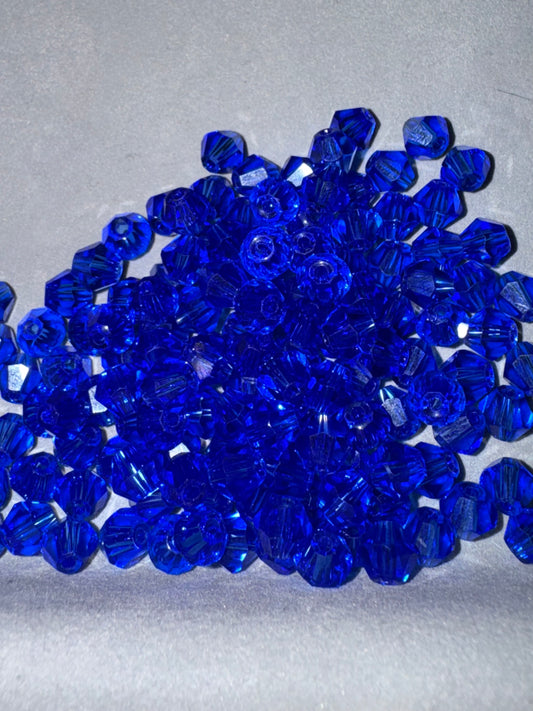 A pile of faceted cobalt blue beads on a light gray textured background.