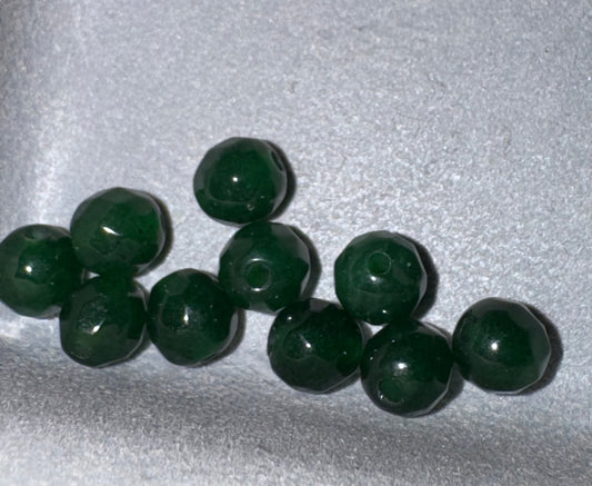 A group of dark green faceted glass beads with a central hole, arranged on a textured light gray background.